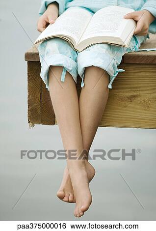 Stock Photograph - Girl sitting on edge of dock, reading book. Fotosearch