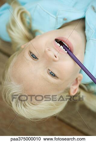 Stock Image - Little girl with head upside down and pencil in mouth. Fotosearch