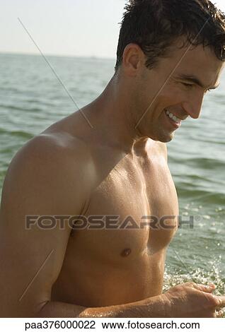Stock Image - Barechested man, sea in background. Fotosearch