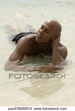 Man lying in shallow water, eyes closed View Large Photo Image Picture - Man lying in shallow water, eyes closed. Fotosearch
