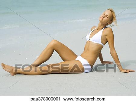 Stock Image - Woman lounging on beach in sun, full length. Fotosearch