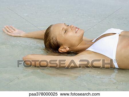 Woman lying in shallow water on beach, eyes closed View Large Photo Image Stock Photography - Woman lying in shallow water on beach, eyes closed. Fotosearch