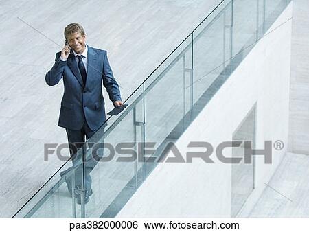 Businessman leaning on railing, using cell phone, high angle view View Large Photo Image Stock Photograph - Businessman leaning on railing, using cell phone, high angle view. Fotosearch