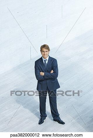 Stock Image - Businessman standing with arms folded, high angle view. Fotosearch