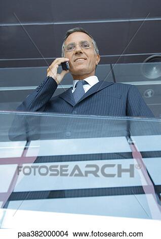 Businessman using cell phone, low angle view View Large Photo Image Picture - Businessman using cell phone, low angle view. Fotosearch