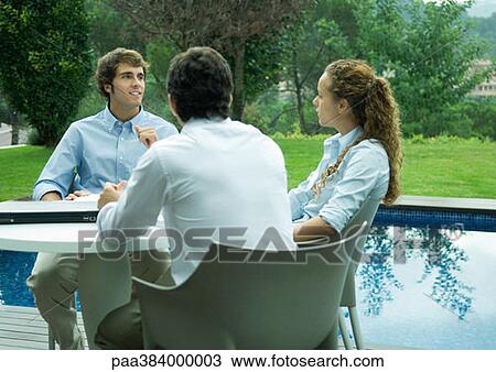 Stock Image - Casually dressed young executives working near edge of pool. Fotosearch