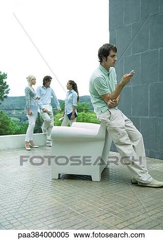 Casually dressed young executives standing on terrace, man in foreground using cell phone View Large Photo Image Stock Photography - Casually dressed young executives standing on terrace, man in foreground using cell phone. Fotosearch