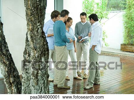 Stock Image - Group of casually dressed adults looking at documents, full length. Fotosearch