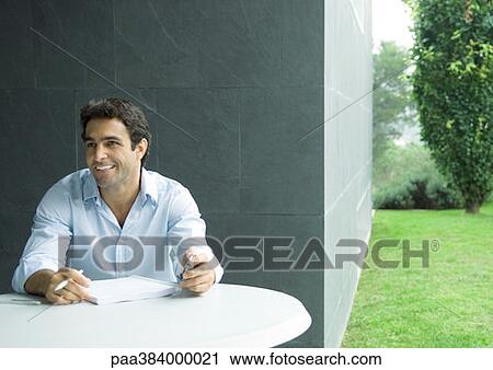 Stock Image - Man sitting at table outdoors, working. Fotosearch