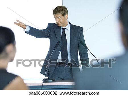 Businessman standing next to microphones, gesturing out of frame View Large Photo Image Stock Image - Businessman standing next to microphones, gesturing out of frame. Fotosearch