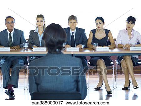 Executives sitting at conference table, looking at man in foreground View Large Photo Image Stock Photo - Executives sitting at conference table, looking at man in foreground. Fotosearch