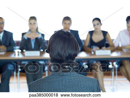 Executives sitting at conference table, looking at man in foreground View Large Photo Image Stock Photo - Executives sitting at conference table, looking at man in foreground. Fotosearch