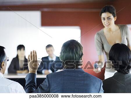 Stock Photo - Executives sitting in seminar, woman holding microphone to man raising hand. Fotosearch