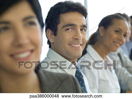Stock Photo - Business associates in a row, one man smiling at camera. Fotosearch
