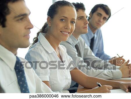 Stock Photograph - Business associates sitting at table, woman smiling at camera. Fotosearch