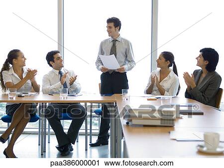 Stock Image - Businesspeople applauding colleague in conference room. Fotosearch