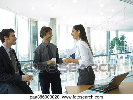 Stock Image - Three office workers standing with cups of coffee, talking. Fotosearch