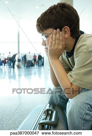 Stock Photo - Boy sitting in airport, holding head. Fotosearch