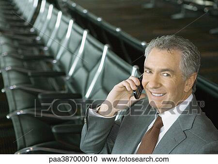 Stock Image - Businessman using cell phone in airport lounge. Fotosearch