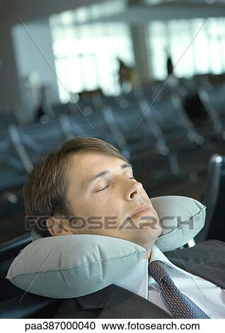 Man resting with neck pillow in airport lounge View Large Photo Image Stock Image - Man resting with neck pillow in airport lounge. Fotosearch