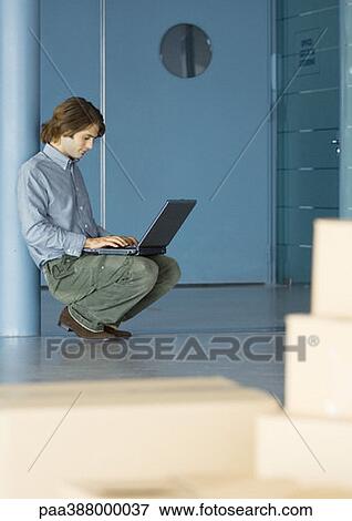 Businessman leaning against pole, using laptop, cardboard boxes in foreground View Large Photo Image Stock Photo - Businessman leaning against pole, using laptop, cardboard boxes in foreground. Fotosearch