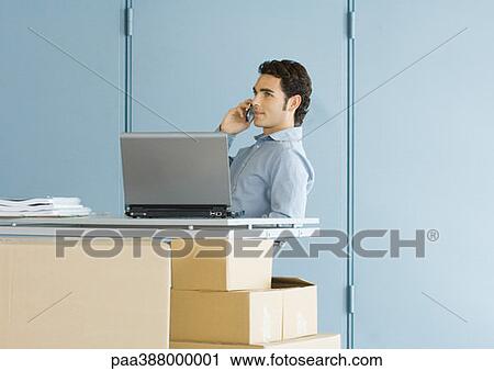 Businessman using cell phone, sitting at table top supported by cardboard boxes View Large Photo Image Stock Image - Businessman using cell phone, sitting at table top supported by cardboard boxes. Fotosearch