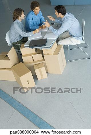 Picture - Businessmen sitting at table top supported by cardboard boxes, high angle view. Fotosearch