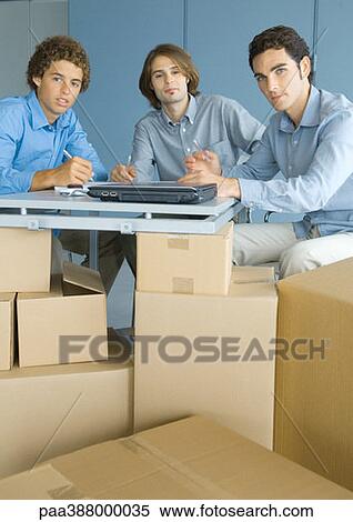 Businessmen sitting at table top supported by cardboard boxes, portrait View Large Photo Image Stock Photography - Businessmen sitting at table top supported by cardboard boxes, portrait. Fotosearch