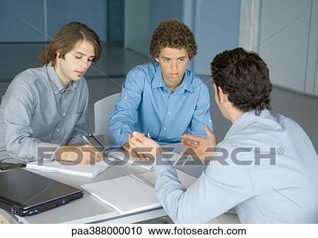Three young business men working at table View Large Photo Image Stock Image - Three young business men working at table. Fotosearch