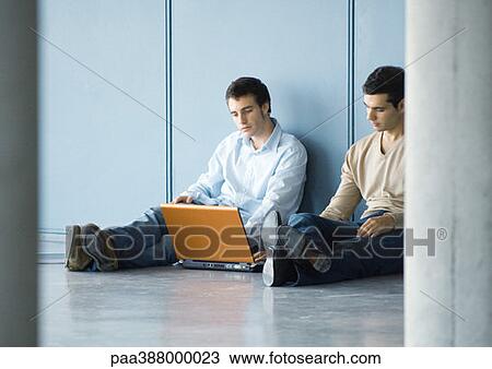 Two young businessmen, sitting on floor, using laptop View Large Photo Image Stock Image - Two young businessmen, sitting on floor, using laptop. Fotosearch