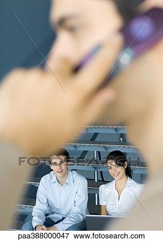 Young business professionals, man using cell phone in blurred foreground View Large Photo Image Stock Photo - Young business professionals, man using cell phone in blurred foreground. Fotosearch
