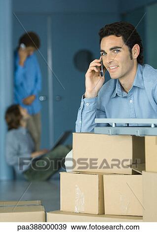 Young businessman using cellphone, sitting at table supported by cardboard boxes View Large Photo Image Stock Photo - Young businessman using cellphone, sitting at table supported by cardboard boxes. Fotosearch