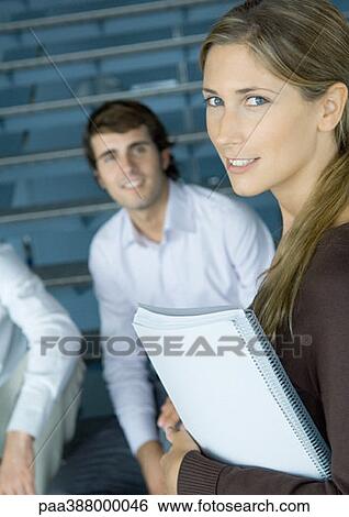 Young businesswoman holding notebook, colleagues in background View Large Photo Image Stock Photograph - Young businesswoman holding notebook, colleagues in background. Fotosearch