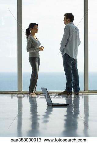 Young man and woman standing face to face by window, laptop on floor, full length View Large Photo Image Stock Image - Young man and woman standing face to face by window, laptop on floor, full length. Fotosearch