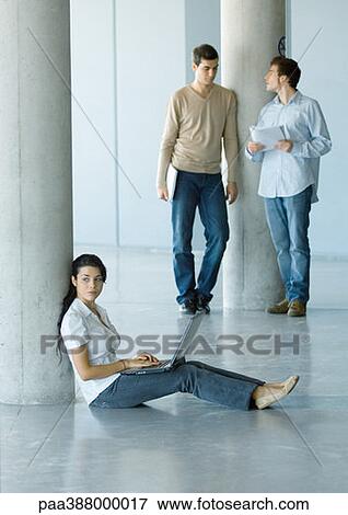Young woman sitting on floor, using laptop, two men standing behind her View Large Photo Image Stock Photo - Young woman sitting on floor, using laptop, two men standing behind her. Fotosearch