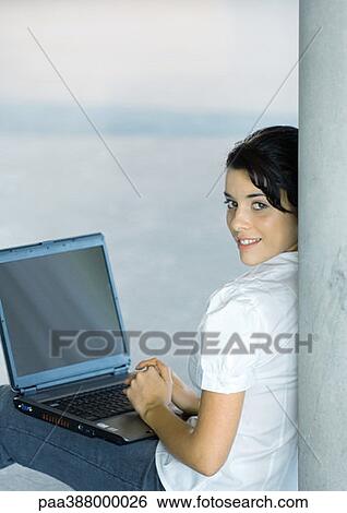 Young woman sitting on floor, using laptop, looking over shoulder at camera View Large Photo Image Stock Photograph - Young woman sitting on floor, using laptop, looking over shoulder at camera. Fotosearch