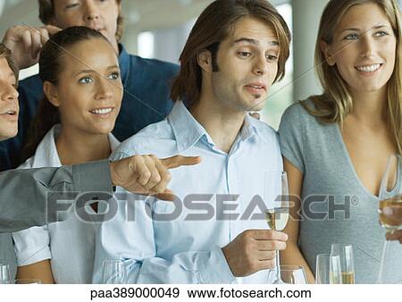 Stock Photo - Group of adults with glasses of champage, one person pointing and another looking down. Fotosearch