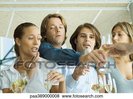Stock Photo - Man reaching over friends' shoulders for glass of champagne. Fotosearch