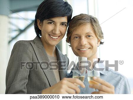 Stock Image - Professional man and woman clinking glasses of champagne, smiling at camera. Fotosearch