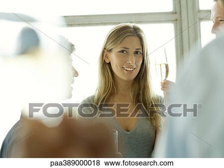 Young woman holding up glass of champagne during office party View Large Photo Image Stock Photo - Young woman holding up glass of champagne during office party. Fotosearch