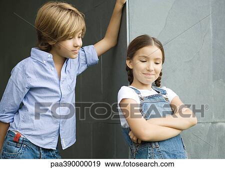 Stock Photo - Boy and girl, boy leaning against wall, girl crossing arms. Fotosearch
