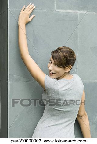 Woman leaning against wall, looking over shoulder at camera, portrait View Large Photo Image Stock Photo - Woman leaning against wall, looking over shoulder at camera, portrait. Fotosearch