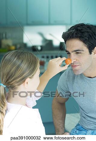 Girl holding up cherry tomato to father's nose View Large Photo Image Stock Image - Girl holding up cherry tomato to father's nose. Fotosearch