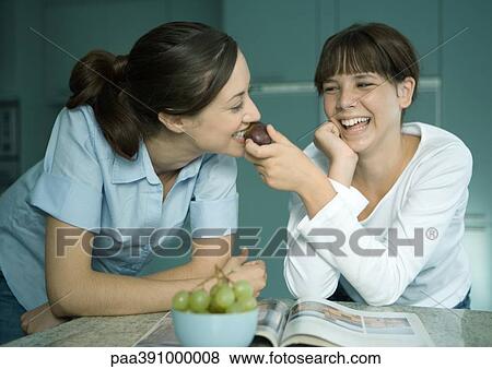 Stock Photo - Mother eating fruit from daughter's hand. Fotosearch