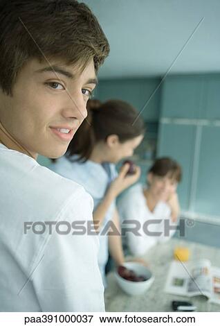 Teenage boy with family in kitchen, looking over shoulder View Large Photo Image Stock Photo - Teenage boy with family in kitchen, looking over shoulder. Fotosearch