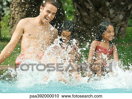 Stock Image - Father and children splashing in swimming pool. Fotosearch