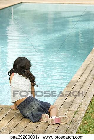 Stock Photo - Little girl sitting by edge of swimming pool, rear view. Fotosearch