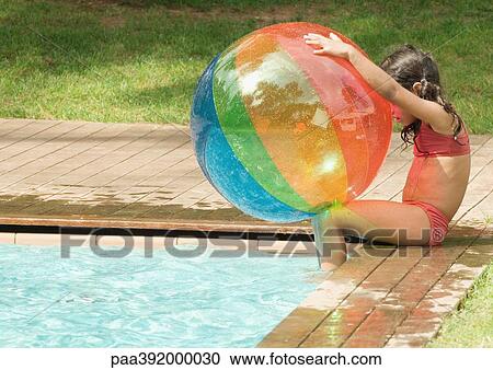 Little girl sitting on edge of swimming pool, holding beach ball View Large Photo Image Stock Image - Little girl sitting on edge of swimming pool, holding beach ball. Fotosearch