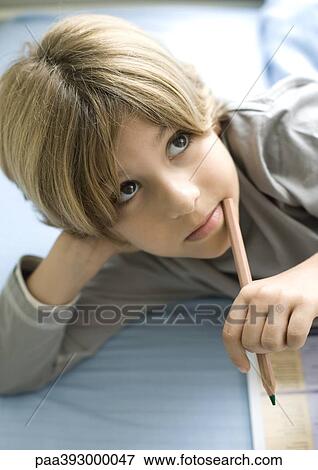 Boy doing homework, holding pencil to mouth View Large Photo Image Stock Photo - Boy doing homework, holding pencil to mouth. Fotosearch