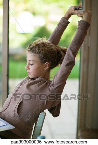 Preteen girl sitting at desk, stretching arms over head View Large Photo Image Stock Photograph - Preteen girl sitting at desk, stretching arms over head. Fotosearch
